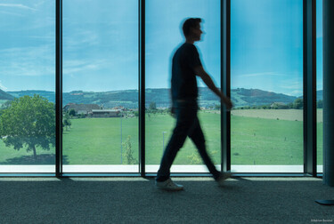 Man walking in front of floor to ceiling smart glass windows overlooking the mountains.