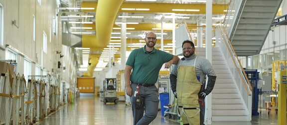 Two coworkers in manufacturing building smiling.