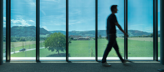 Man walking in front of floor to ceiling smart glass windows overlooking the mountains.